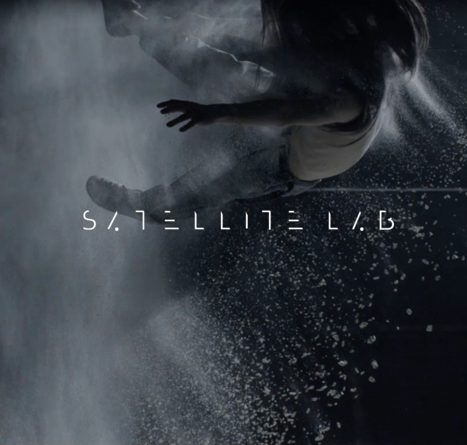 Satellite Lab wordmark over a film still with a figure and suspended particles