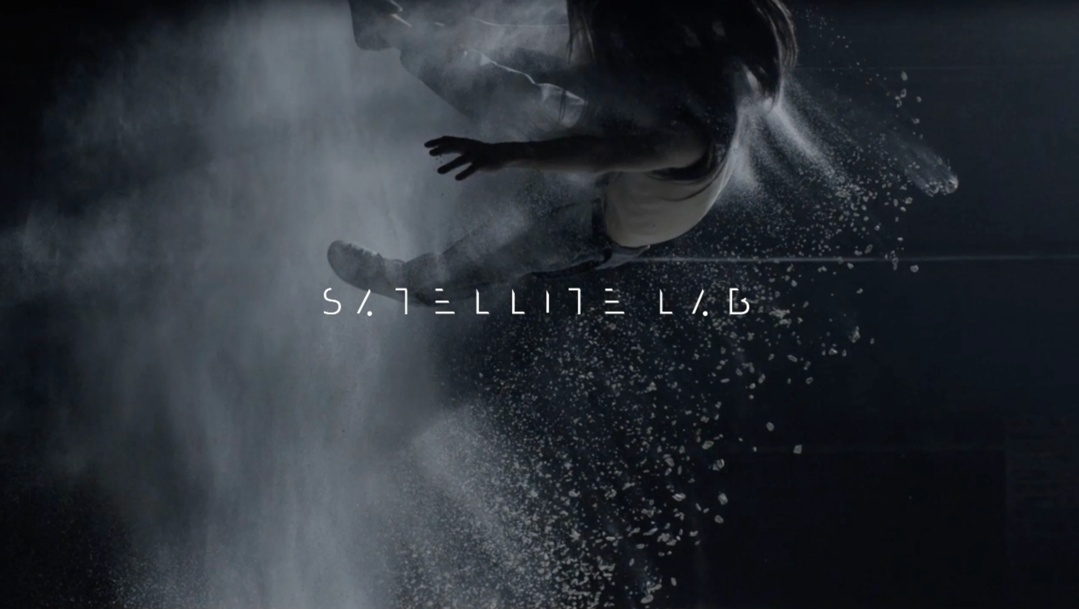 Satellite Lab wordmark over a film still with a figure and suspended particles